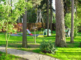 Стандартное оборудование для детской площадки разместили на изумрудной зелени газона так, чтобы и из дома можно было наблюдать за детьми