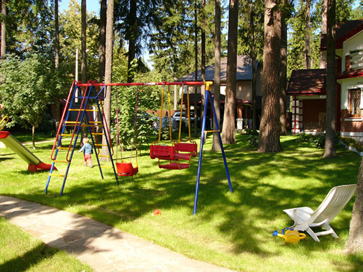 Стандартное оборудование для детской площадки разместили на изумрудной зелени газона так, чтобы и из дома можно было наблюдать за детьми.