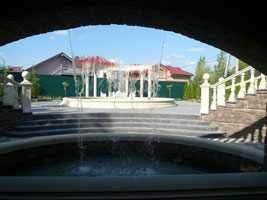 Вид из грота сквозь водопад на фонтан и площадку для отдыха у фонтана 